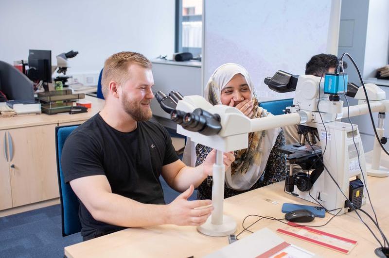 Students at the Royal London Hospital, laughing next to a microscope